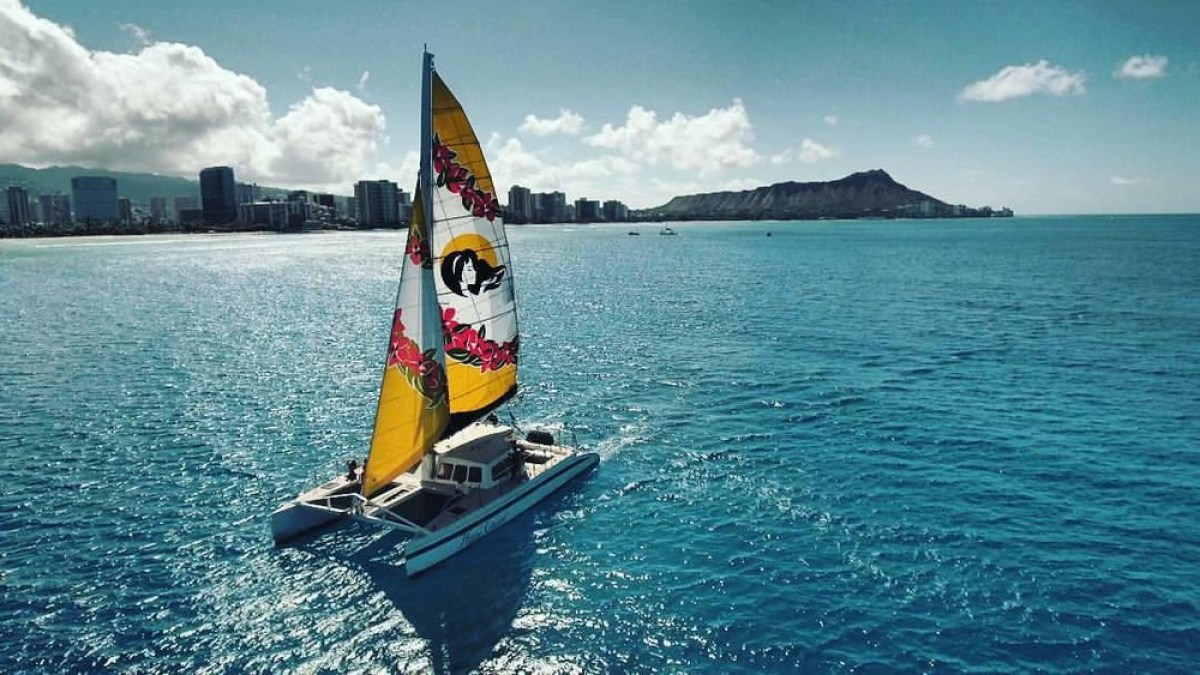 Catamaran sailing in blue ocean with city skyline and mountain in background.