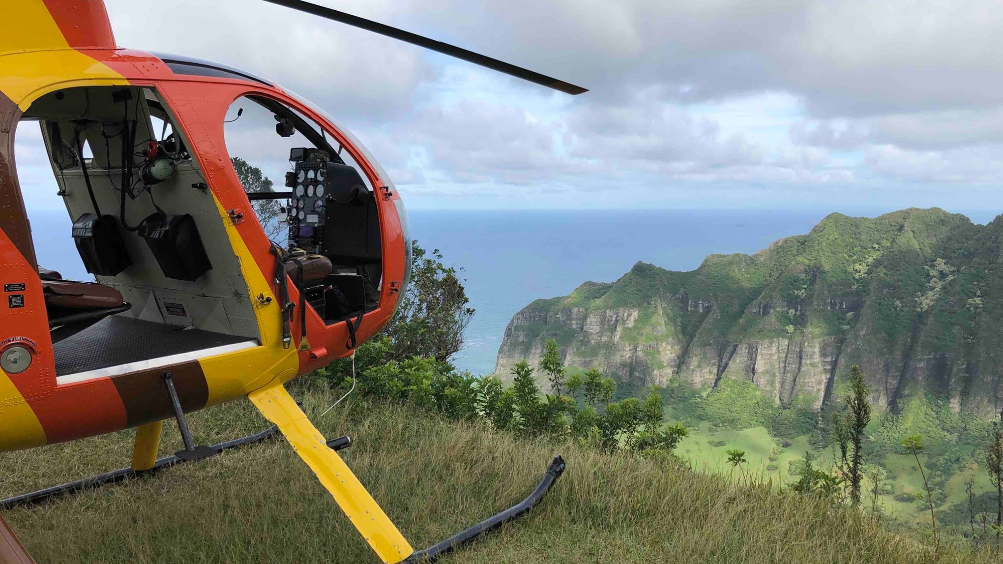 Helicopter on grassy cliff with view of ocean and lush green cliffs in background.
