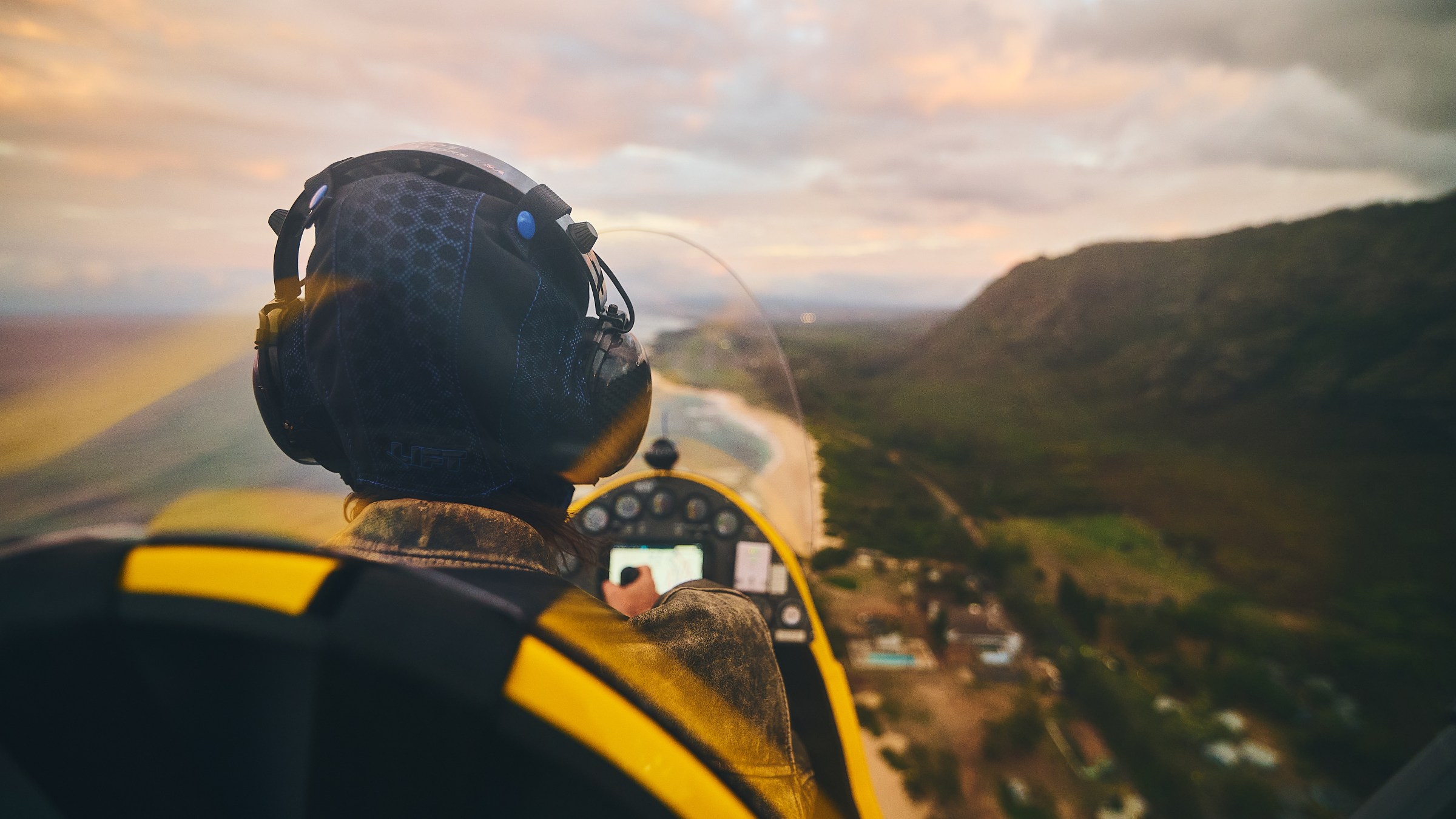 Person flying a small plane over a coastal landscape at sunset.