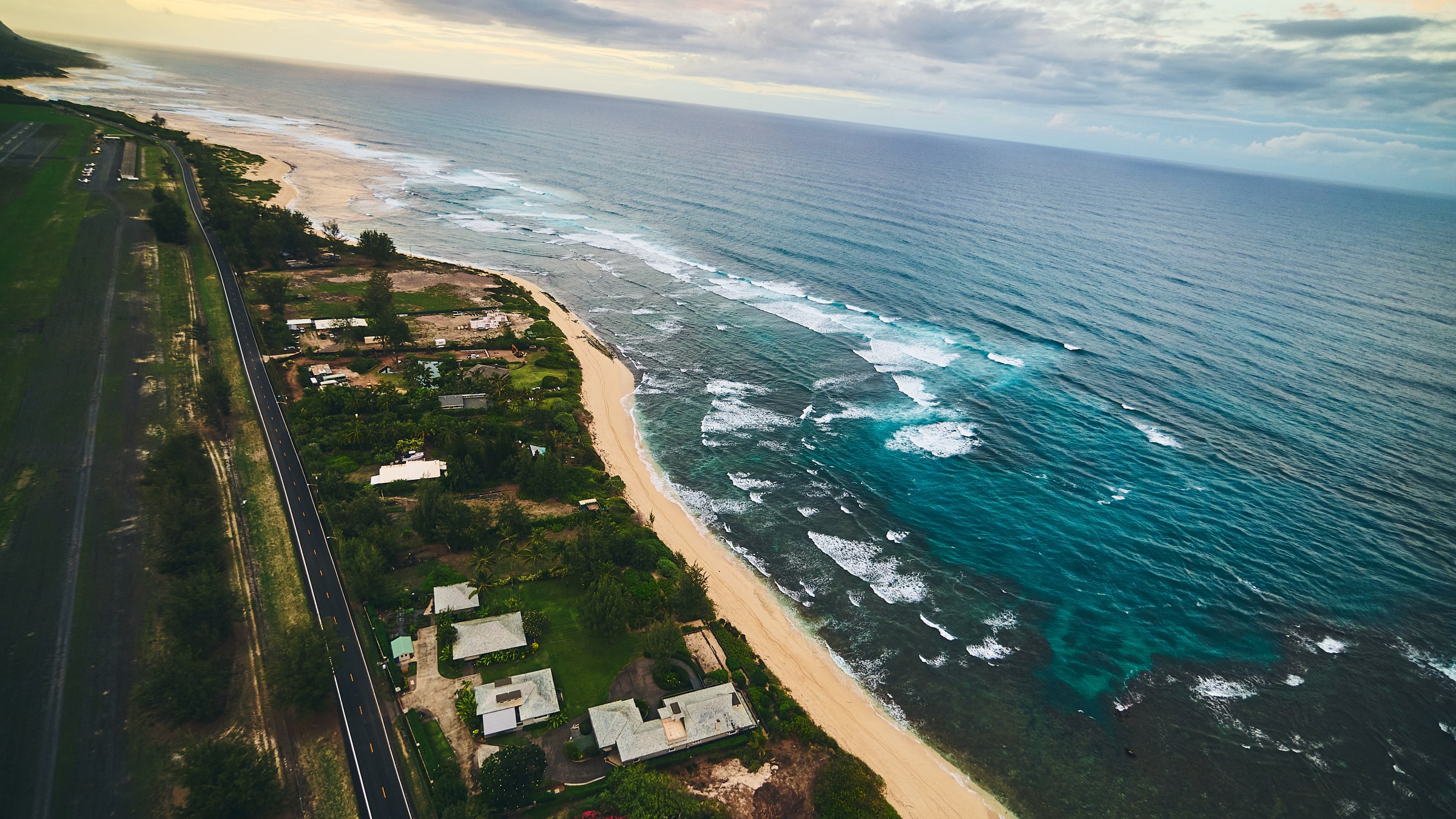Aerial view of a coastal road with houses, beach, and ocean waves.