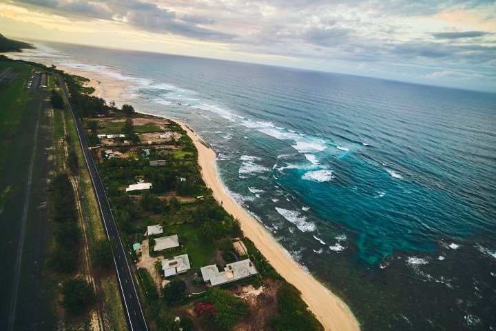 Aerial view of a coastal road with houses, beach, and ocean waves.