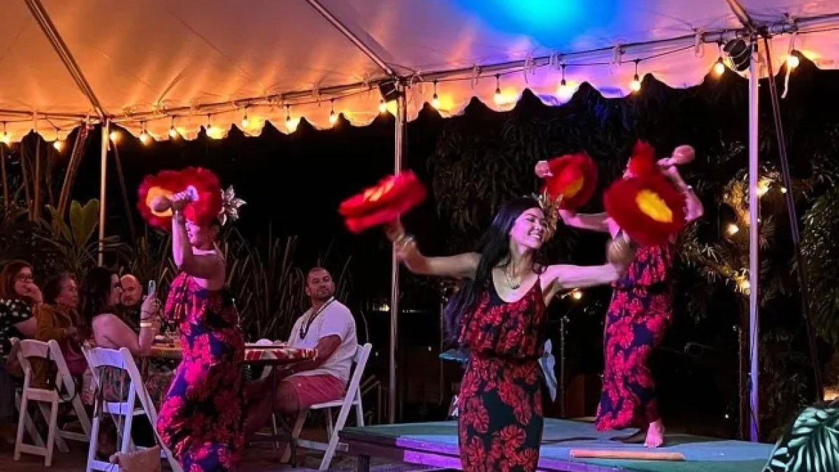 Dancers in red and black dresses perform with red fans under a lit canopy at night.