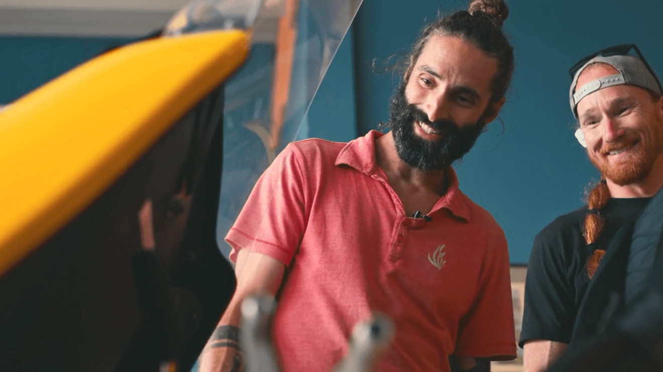 Two men smiling and looking at a yellow object indoors.
