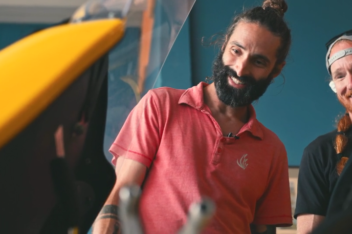 Two men smiling and looking at a yellow object indoors.