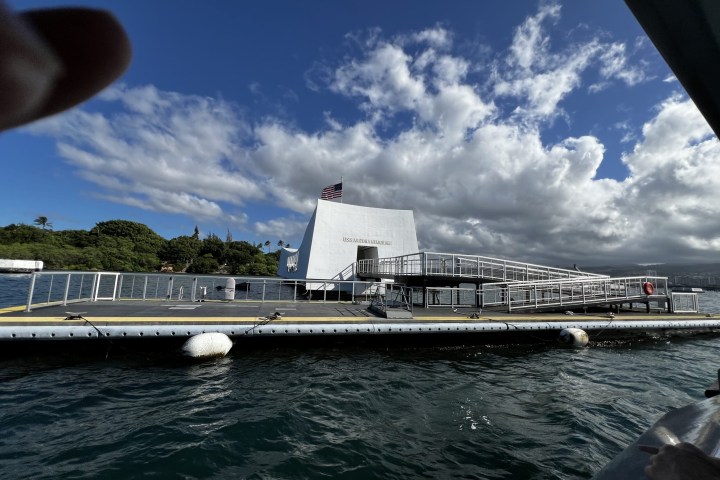 White memorial structure on water with American flag under a partly cloudy sky.