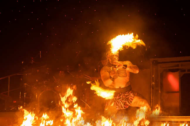 Performer twirling flaming sticks in a dramatic fire dance on stage.
