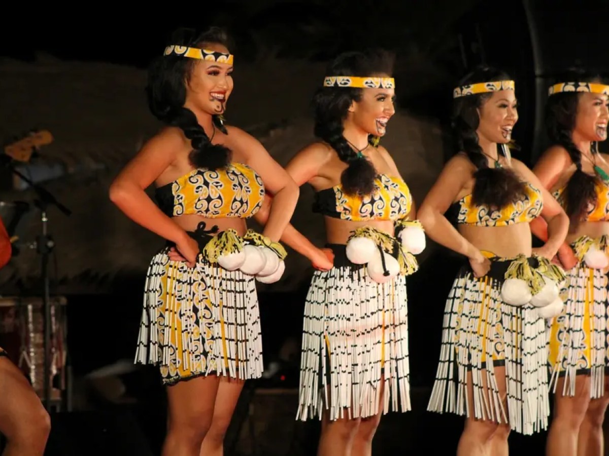 Four women in traditional Polynesian attire perform a dance on stage.