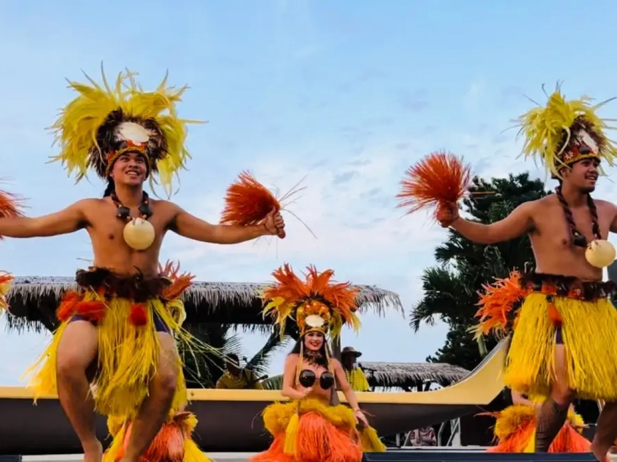Dancers in traditional costumes performing a cultural dance with palm trees in the background.