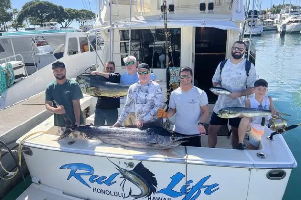 Group of seven people on a boat with caught fish, including a large marlin.