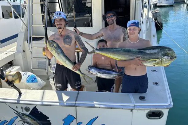 Four people on a boat holding large fish, smiling.