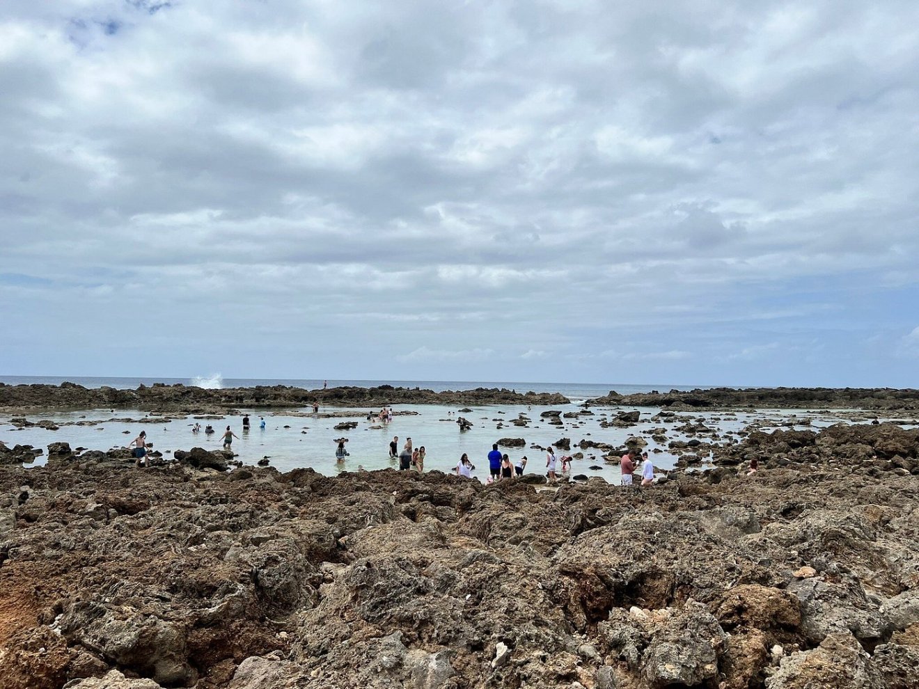 People exploring rocky tidal pools under a cloudy sky.