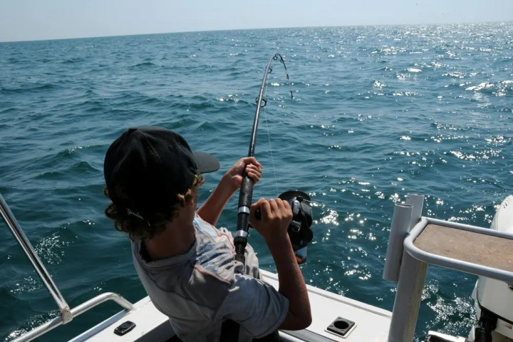 Person fishing on a boat in the ocean, holding a fishing rod.